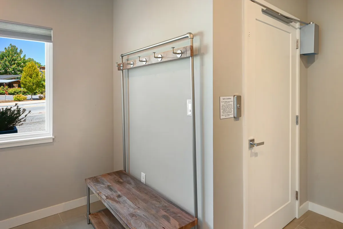 An inviting foyer with a wooden bench and coat rack positioned near a window, bathed in natural light. The scene reflects a welcoming entryway where guests can hang coats or pause before heading further inside.