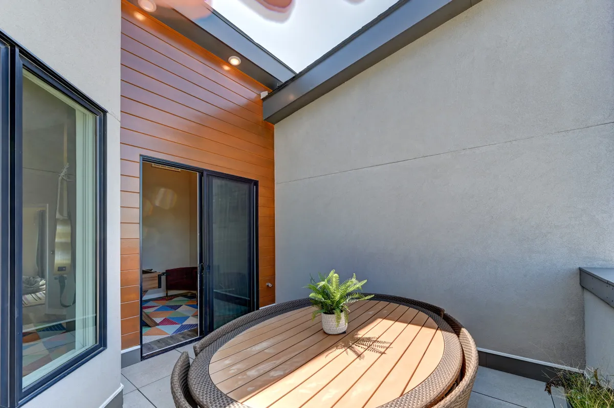 An inviting round wooden table with a green plant sits near a sliding glass door, allowing sunlight to stream into the space. The setup suggests a spot for casual dining, morning coffee, or conversation, with easy indoor-outdoor flow that ties into the idea of starting the day together or winding down after exploring.