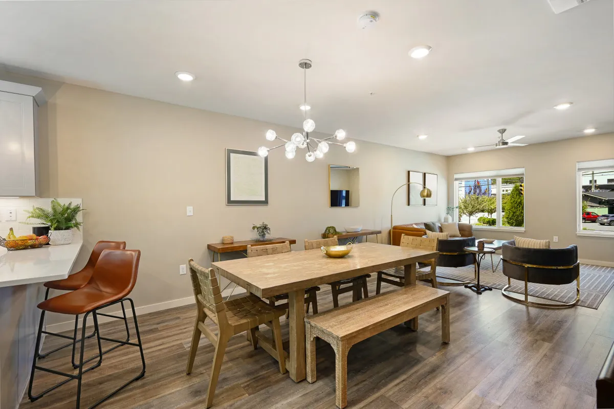 A bright dining area with a large table, elegant chandelier, comfortable seating, and expansive windows offering city views. The space is set for family meals or social gatherings, with natural light creating a welcoming and comfortable mood.